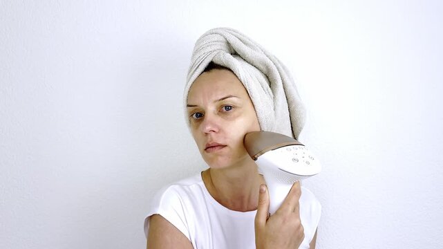 Close up of female holding pulsed light laser machine near cheek for skincare lift therapy. Domestic body care routine, youth look and cosmetology