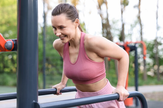Athletic woman exercising on parallel bars at outdoor gym