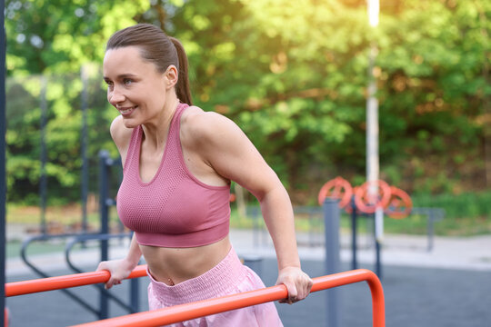 Athletic woman exercising on parallel bars at outdoor gym