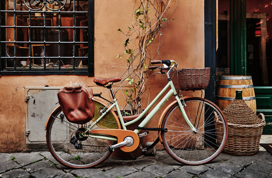 sage green vintage city bicycle with a wicker front basket and leather saddlebag against a tan wall, Rome, Italy, Europe