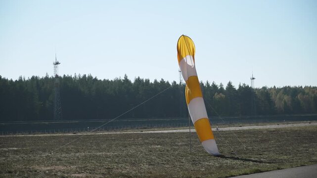 Bright striped windsock on aerodrome lying calmly on ground. Airport indicator of wind strength and direction resting on aerodrome grass during absence of wind.