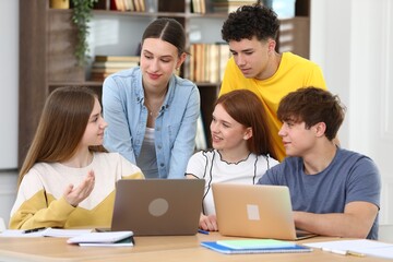 Fototapeta premium Group of students studying with laptops and notebooks at wooden desk in classroom