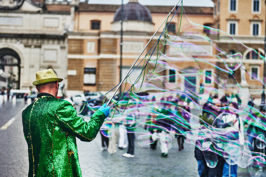 street performer creating massive soap bubbles for tourists and locals in Piazza del Popolo, a grand, historic neoclassical square, Rome, Italy, Europe 