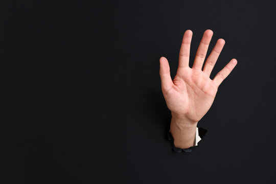 Man showing palm through hole in black paper, closeup. Space for text