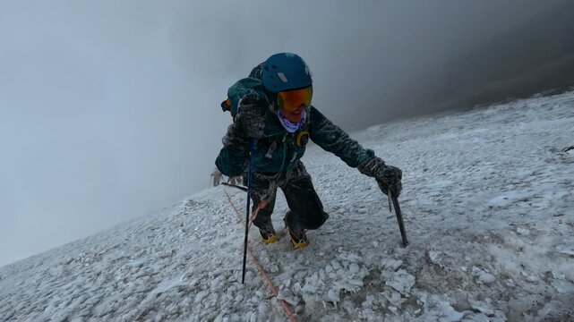Alpinist with an ice axe and crampons climbing a steep icy slope during a winter storm
