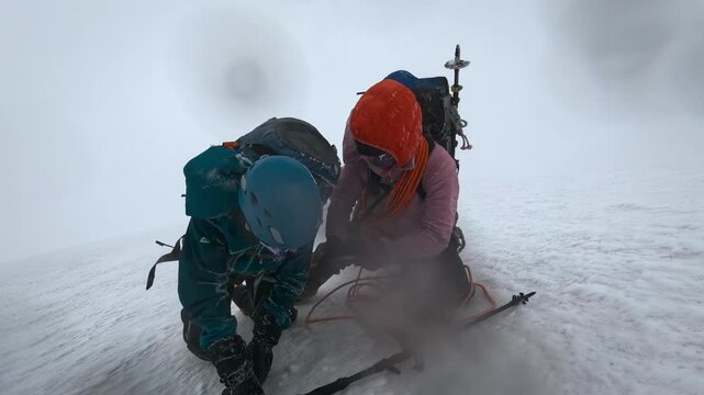 Two alpinists struggle against a snowstorm while climbing a dangerous, icy mountain slope