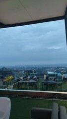 Fototapeta premium View from a modern rooftop cafe terrace overlooking a vast city skyline under a dramatic overcast evening sky.