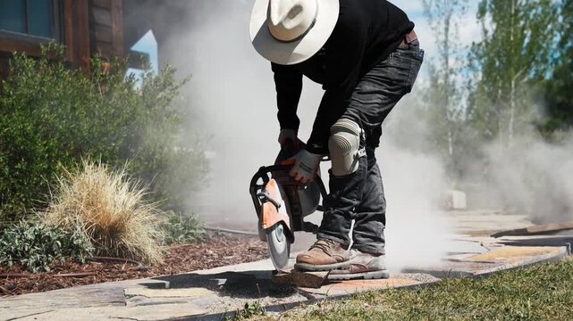 Construction worker operating a concrete saw cutting stone pavers with thick dust cloud 4k
