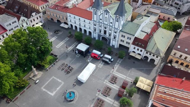 Cinematic aerial drone footage of Mari&aacute;nske N&aacute;mestie in the historic center of Žilina, Slovakia, featuring the Church of the Conversion of Saint Paul, surrounding architecture, urban square, rooftops,