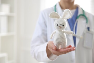 Pediatrician holding toy bunny in clinic, closeup. Space for text