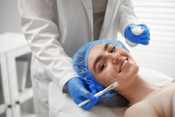 Naklejka premium Beautician in medical gloves applying chemical peel with makeup brush onto client's face in salon, closeup