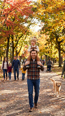 Fototapeta premium Happy father giving shoulder ride to little son walking in autumn park