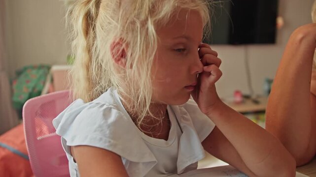 Child looking at laptop with low concentration while working on assignment, mother supporting learning process at home