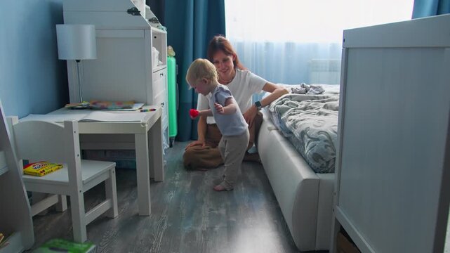 Little child learning to walk indoors with mother. First steps and early childhood milestone at home