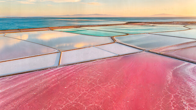 Vibrant pink and turquoise salt evaporation ponds reflecting the sky at sunset