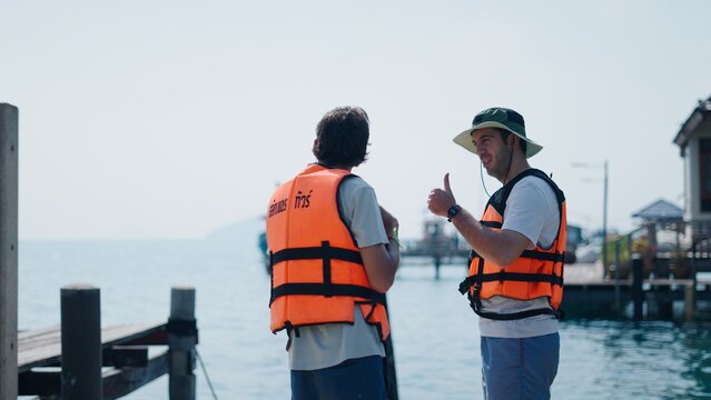Tourists wearing life jackets on a dock, one man giving a thumbs up gesture