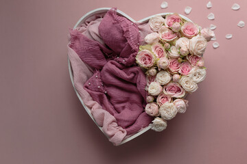 A heart-shaped box decorated with pink roses and fabric on a pink background. A newborn photo session basket. © Svetlana