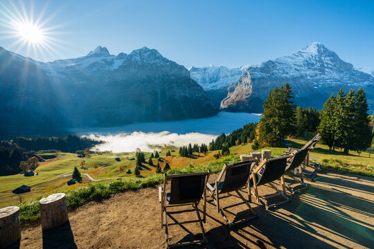 Wooden lounge chairs facing Grindelwald valley cloud sea and Swiss Alps peaks. Switzerland Grindelwald First Bort.