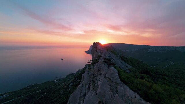 Flying over a mountain range against the background of the setting sun. The sea is visible below. High quality 4k footage FPV drone shoot