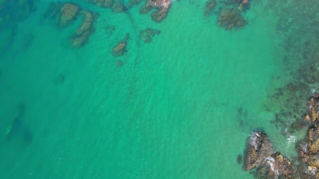 High angle bird's eye view of crystal clear turquoise ocean water with coral reefs and underwater rocks. Beautiful natural sea surface texture for summer travel or abstract background.