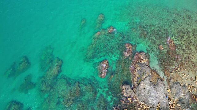 High angle bird's eye view of crystal clear turquoise ocean water with coral reefs and underwater rocks. Beautiful natural sea surface texture for summer travel or abstract background.