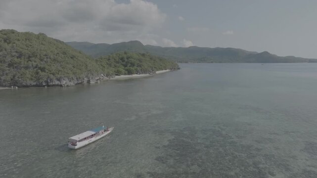 Cinematic aerial drone shot of traditional boat sailing on tropical turquoise ocean water near green island hills in Indonesia, slow motion b-roll. drone, d-log, mavic 3