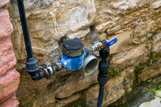 Outdoor water meter with pipes and valve on stone wall
