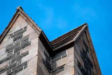 Obraz premium Two towers of a vintage church standing corner to corner. The blocks are beige with decorative old grey stone. The peaked roof is covered with antique slate. The blocks are limestone and granite.