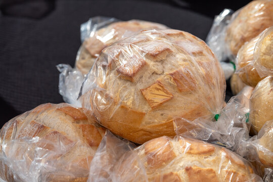 A display of artisan breads in clear plastic bags for sale at a farmer's market. The crusty, sourdough, pumpernickel, white, whole wheat, and traditional homemade rustic loaves are on display for sale