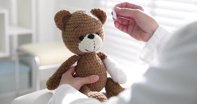Pediatrician putting adhesive bandages onto teddy bear in clinic, closeup