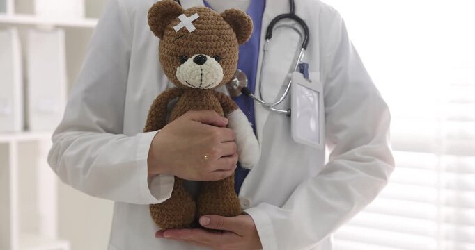 Pediatrician holding teddy bear with adhesive bandages in clinic, closeup