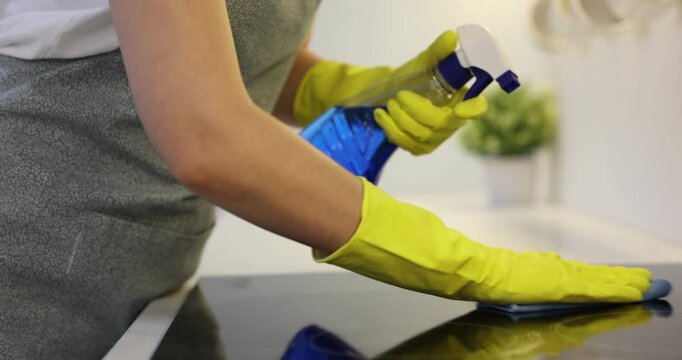 Spring cleaning. Woman in rubber gloves wiping electric stove with rag and bottle of detergent in kitchen