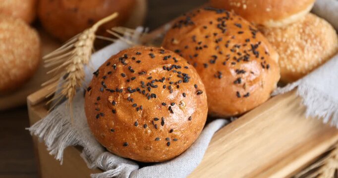 Woman putting bun with sesame seeds into wooden box at table, closeup
