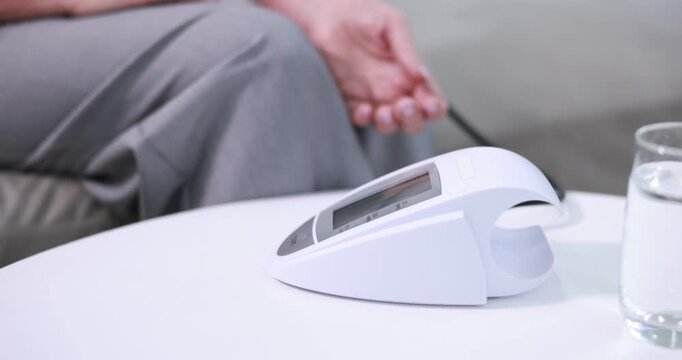 Senior woman measuring blood pressure on sofa at white table indoors, closeup. Camera moving forward