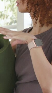 Vertical video: Preparing for yoga, woman wearing tank and pink watch adjusting green mat by window