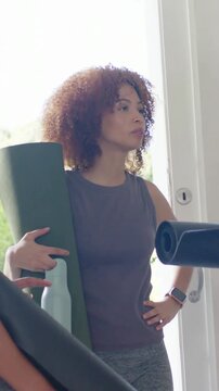 Vertical video: Holding mat, woman responding to friend, talking and gesturing at door in grey top