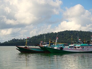 Naklejka premium Traditional fishing boats anchored in the calm coastal waters with the pristine Suwangi Island in the background and clear skies and clouds.