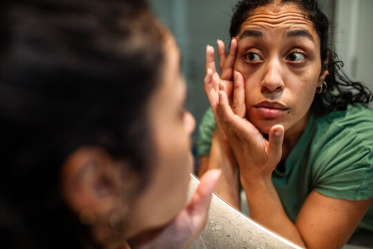 Young woman checking under-eye skin in bathroom mirror