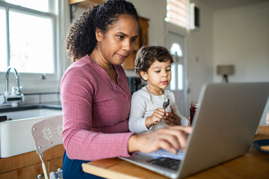 Mother working on laptop with toddler at kitchen table