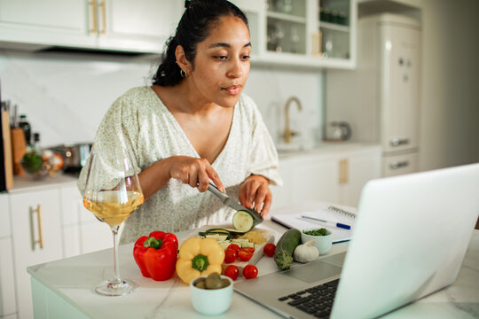 Woman cooking with laptop in bright home kitchen