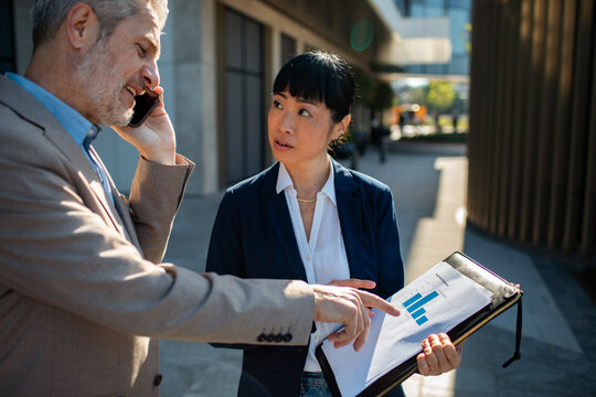 Two business colleagues review sales chart outside office