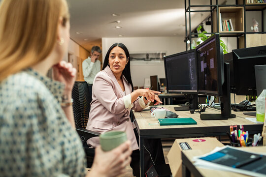 Manager mentoring colleague at dual monitors in modern office