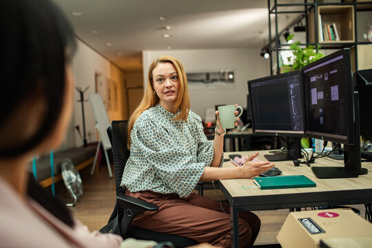 Woman designer mentoring coworker at dual monitors in modern office