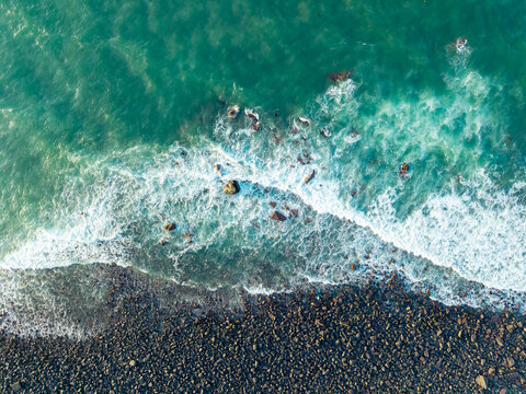 Aerial view of turquoise ocean waves crashing against a pebble stone beach in Pingtan Fujian China