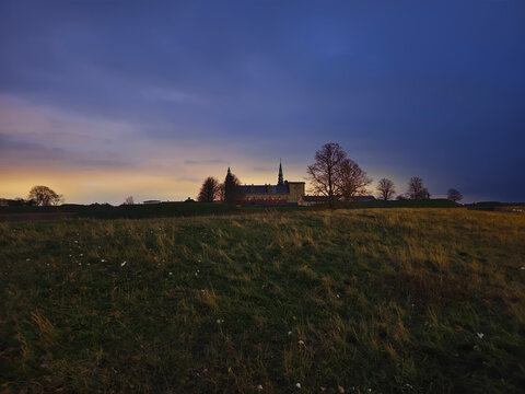 Wide-angle distant view of historic Kronborg Castle surrounded by bare trees and an open grass field at twilight in Denmark