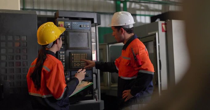 Technicians review machine setup with a clipboard beside a production workstation during quality control in an auto parts assembly factory, showing teamwork, inspection, and process verification.
