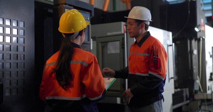 Technicians review machine setup with a clipboard beside a production workstation during quality control in an auto parts assembly factory, showing teamwork, inspection, and process verification.
