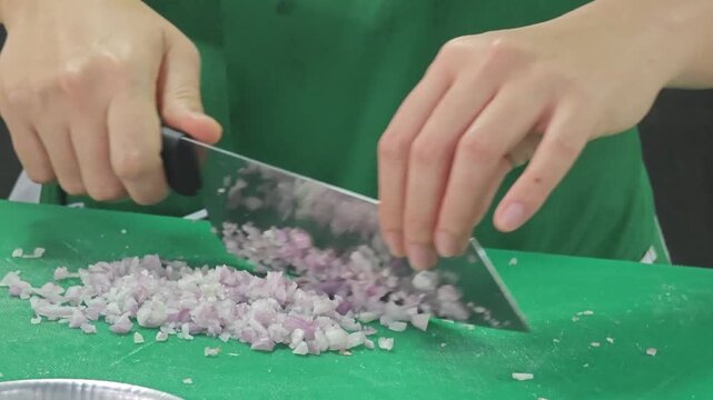 Mincing shallots with a large kitchen knife on a green board.