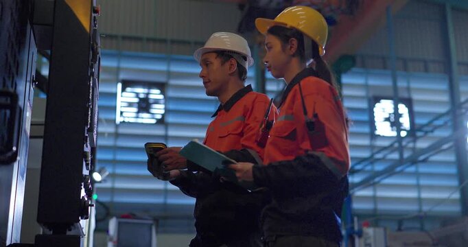 Technicians review machine setup with a clipboard beside a production workstation during quality control in an auto parts assembly factory, showing teamwork, inspection, and process verification.
