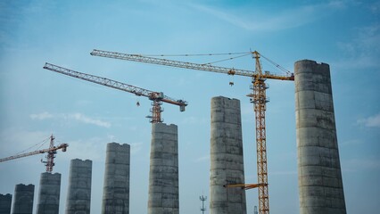 Fototapeta premium Tower cranes and piers at construction site under blue sky